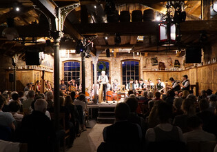Konzertszene mit Musikern in Tracht und aufmerksamen Zuschauerinnen und Zuschauern. | © Hans Fuchs