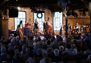 Gruppe von Musikern auf der Bühne, Publikum im Vordergrund. | © Hans Fuchs