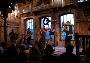Blick in einen vollbesetzten Saal mit Bühne und Musikgruppe im Hintergrund. | © Hans Fuchs